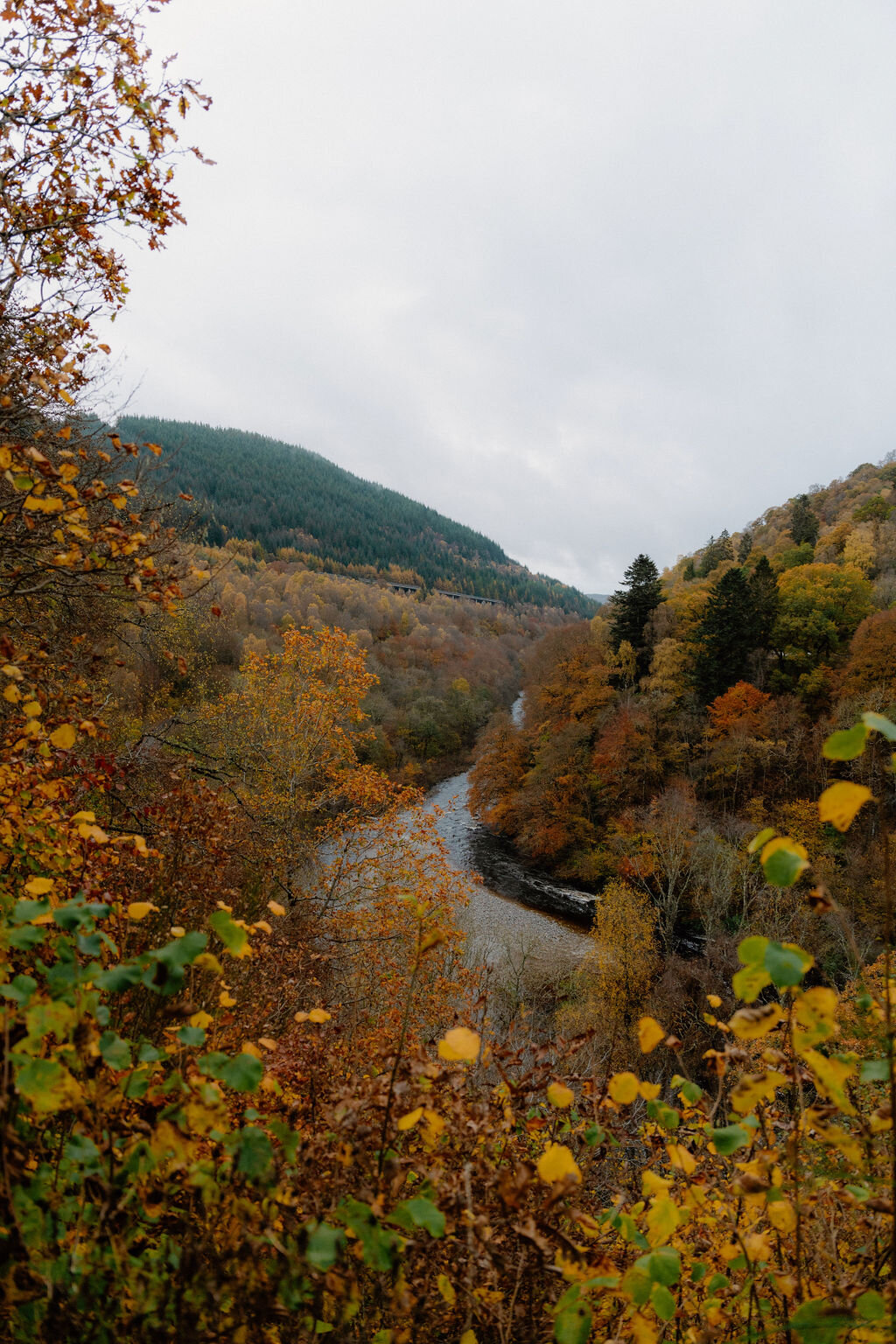 A river winds through an autumn-coloured valley beneath misty hills.