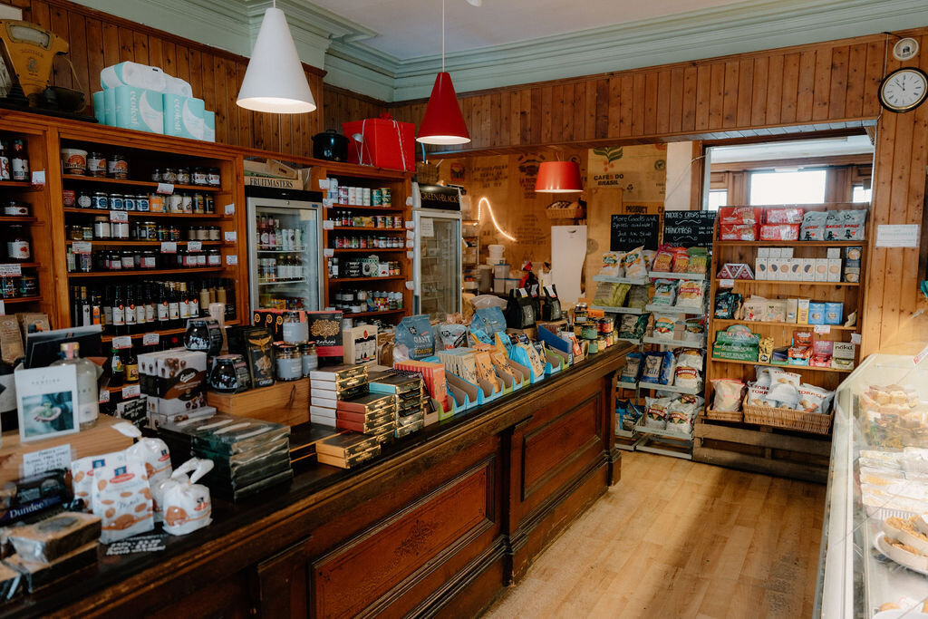 Jars, tins and baked goods fill a wood-panelled shop's counter beneath red and white pendant lights.