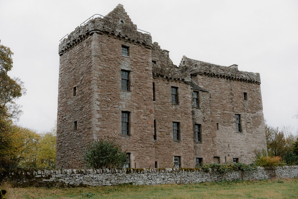A ruined stone tower house stands amid autumn trees in an open field.