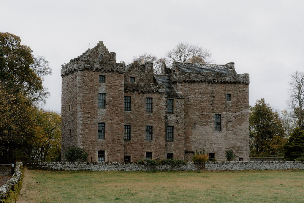 A ruined roofless stone tower house stands in an open field bordered by a dry-stone wall.