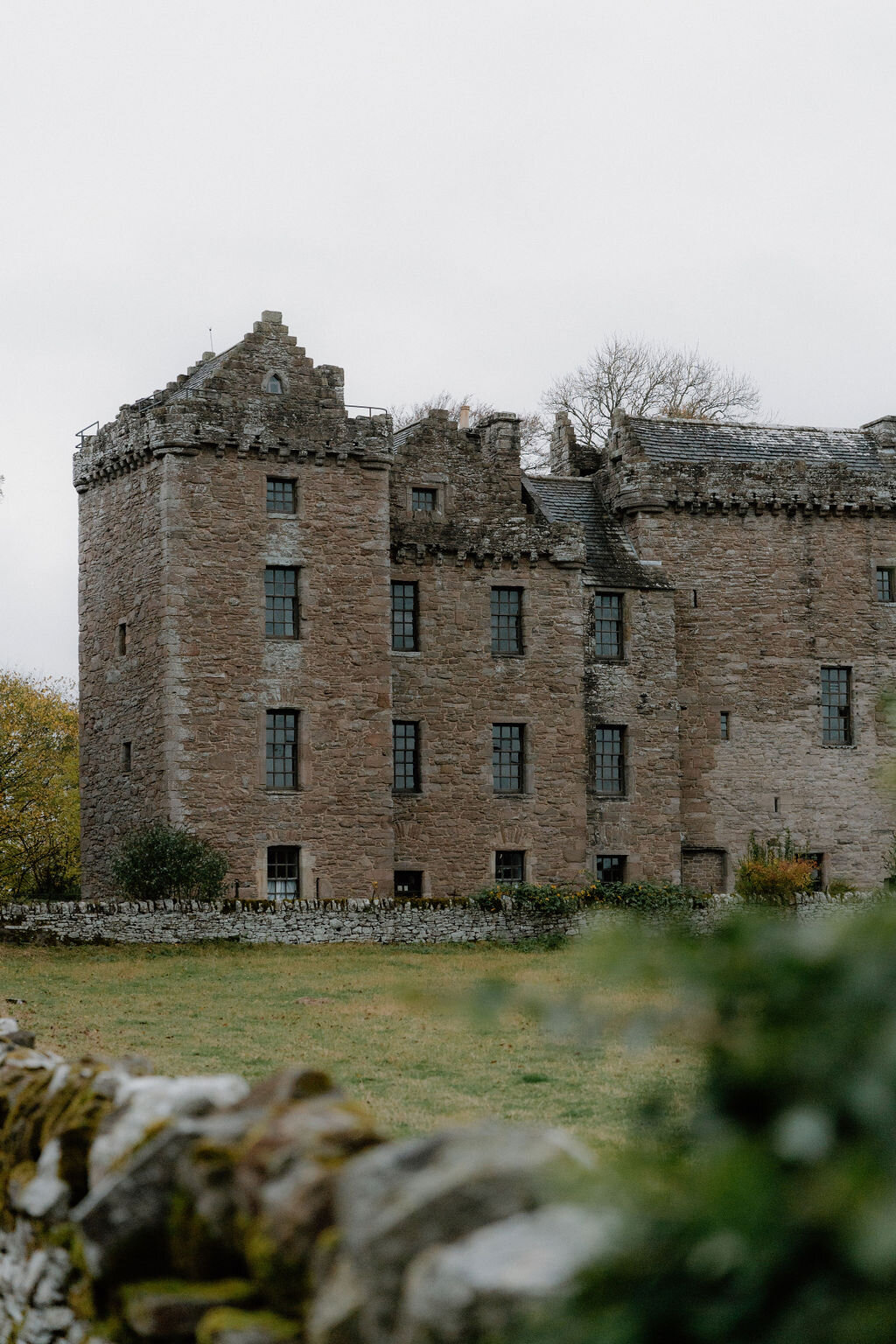 A ruined roofless stone tower house stands beside autumn-coloured trees.