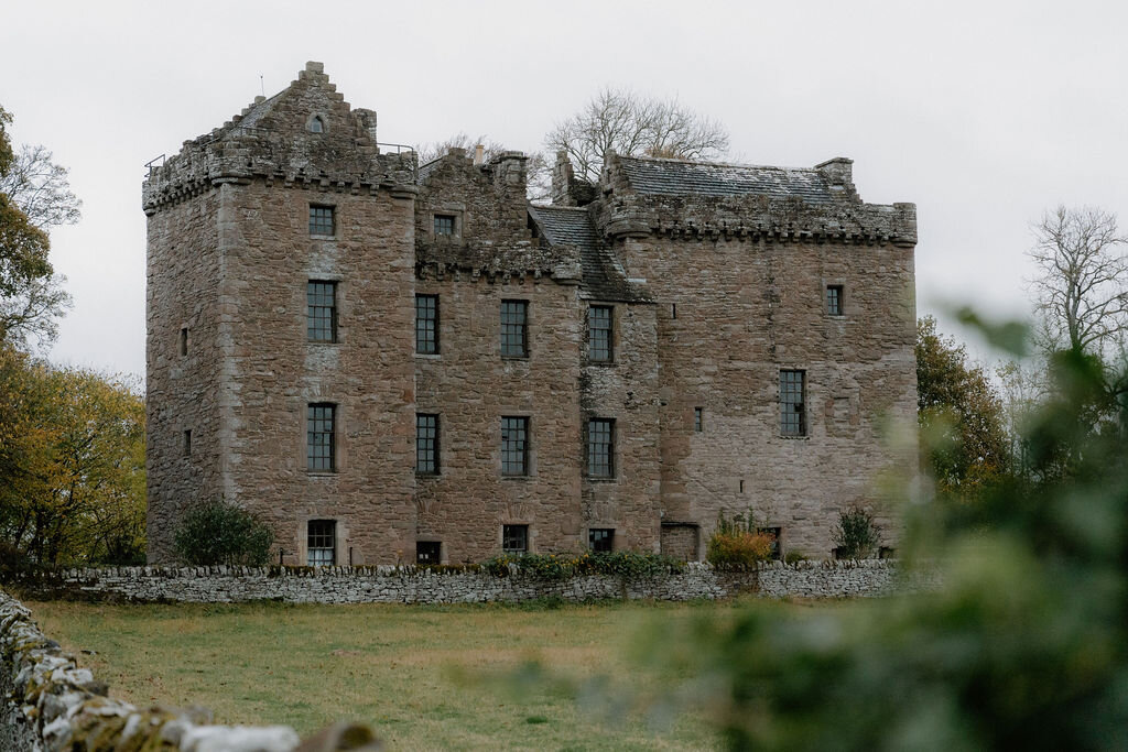 A ruined roofless stone tower house stands beside autumn-tinged trees.