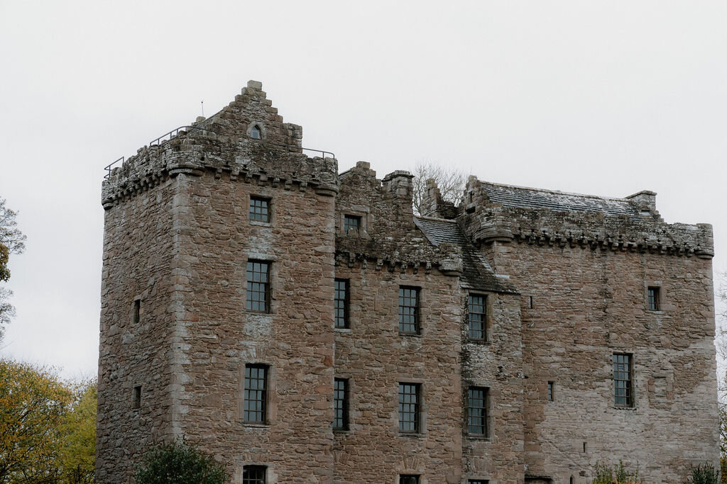 A ruined roofless stone tower house rises above a grassy field.