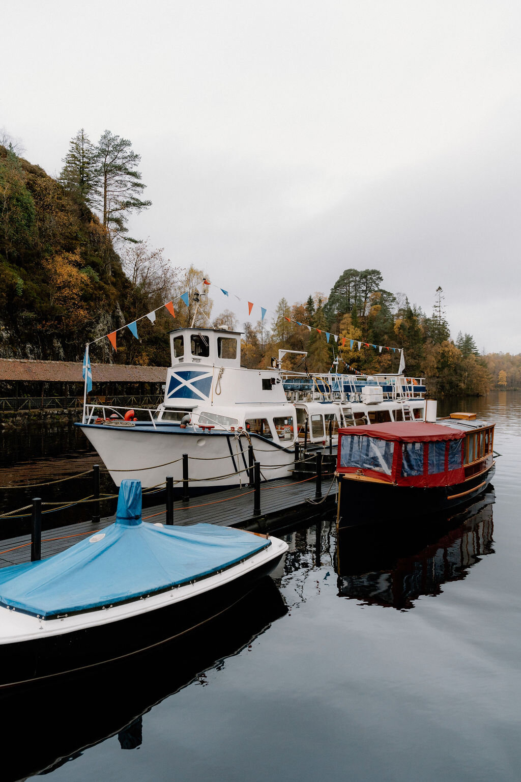 Tour boats moor at a wooden pontoon near Wildwoodz, bunting strung between their masts and autumn trees lining the far bank.