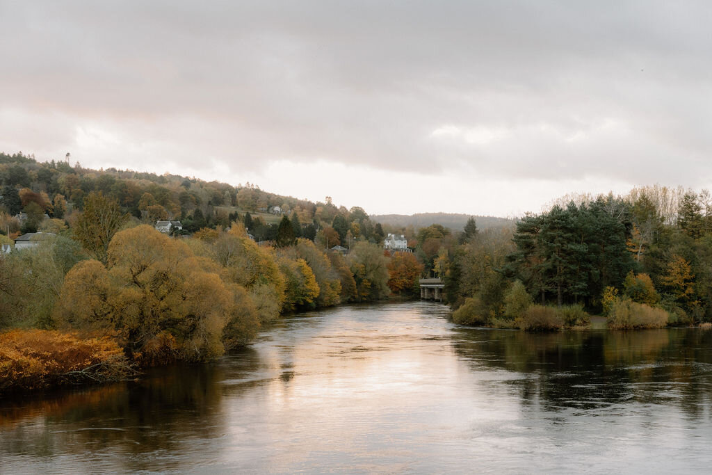 A wide river bordered by autumn trees, a village visible on the far bank.