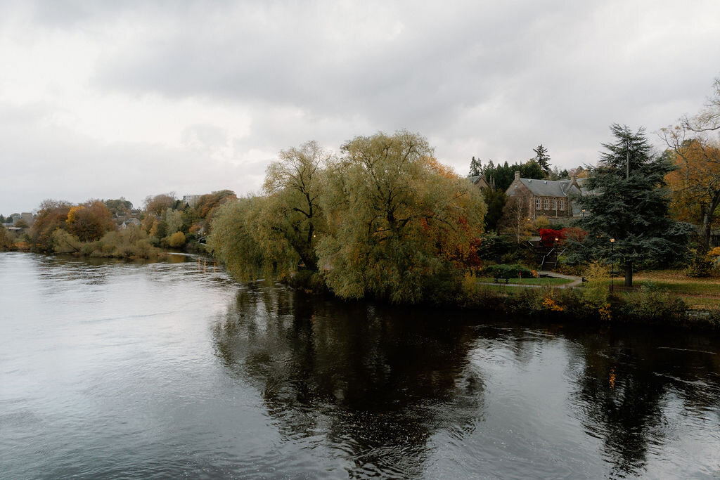 A river bordered by autumn willow trees, a house glimpsed through the branches.