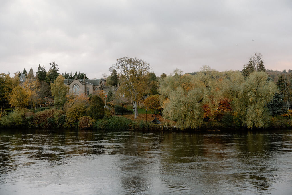 A river bordered by a church and autumn willow trees.