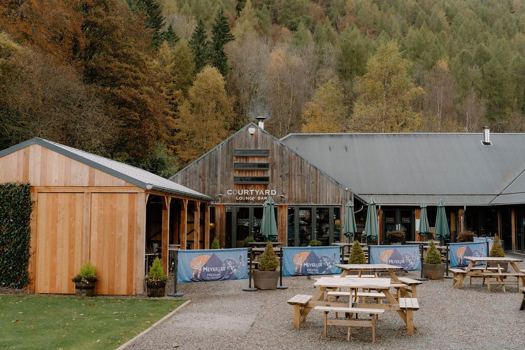 Wildwoodz's "Courtyard" building, picnic tables and banners set out before its timber-clad walls.