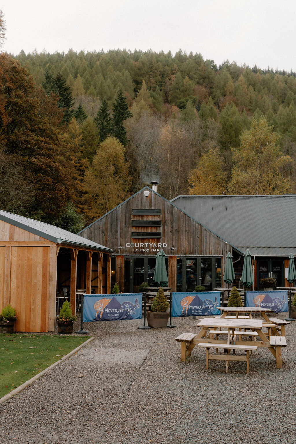 Wildwoodz's Courtyard Lounge Bar, a timber-gabled building with its own sign, picnic tables and striped banners set against autumn woodland.