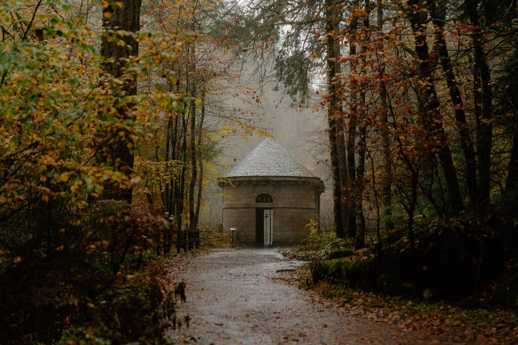 A small domed stone pavilion stands at the end of a path through misty autumn woodland.