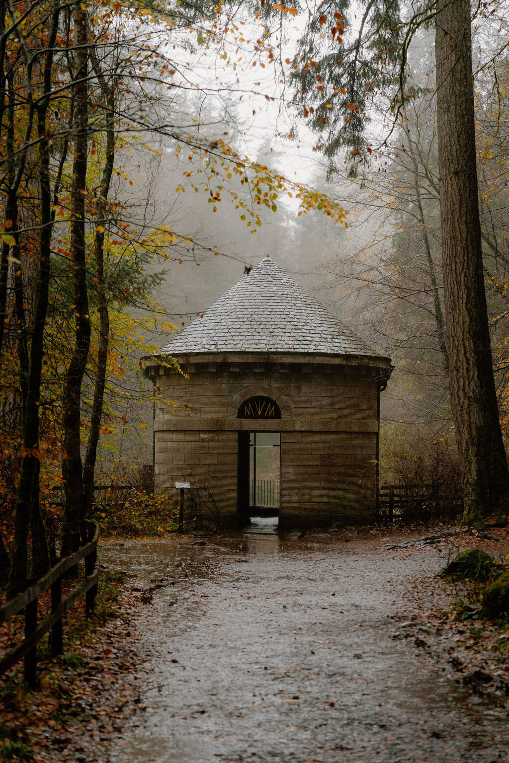 A small domed stone pavilion stands at the end of a path through misty autumn woodland.