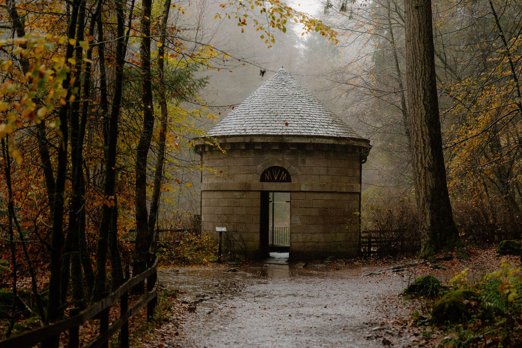 A small domed stone pavilion stands at the end of a path through misty autumn woodland.