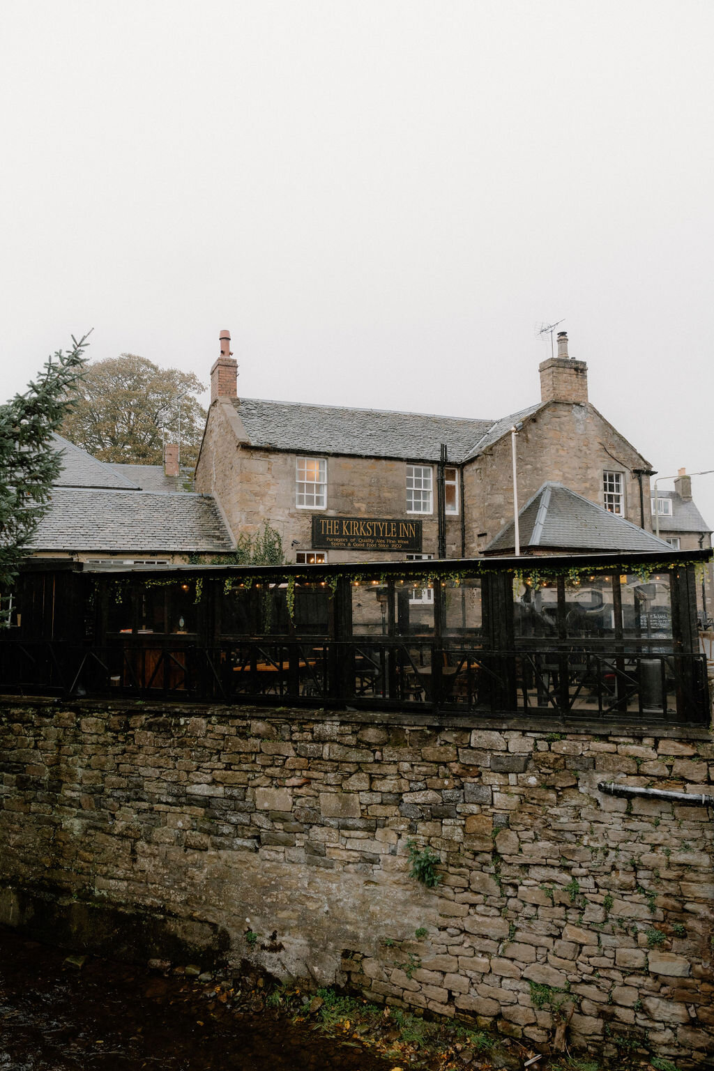 The Kirkstyle Inn's own sign hangs above a covered terrace, stone walls enclosing the garden.