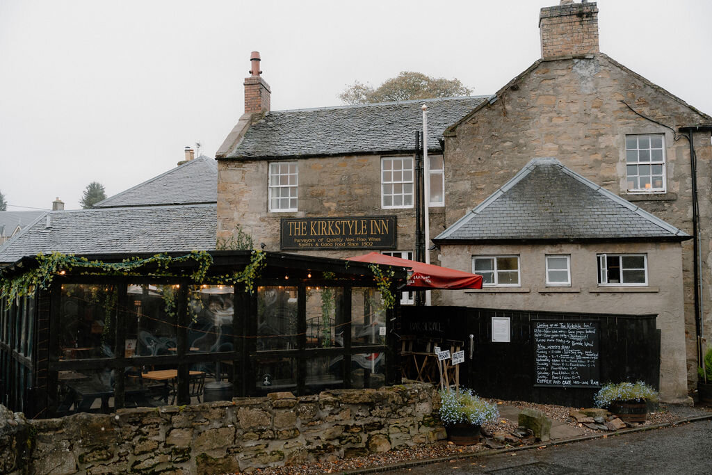 The Kirkstyle Inn's own sign hangs above a covered terrace, stone walls enclosing the garden.