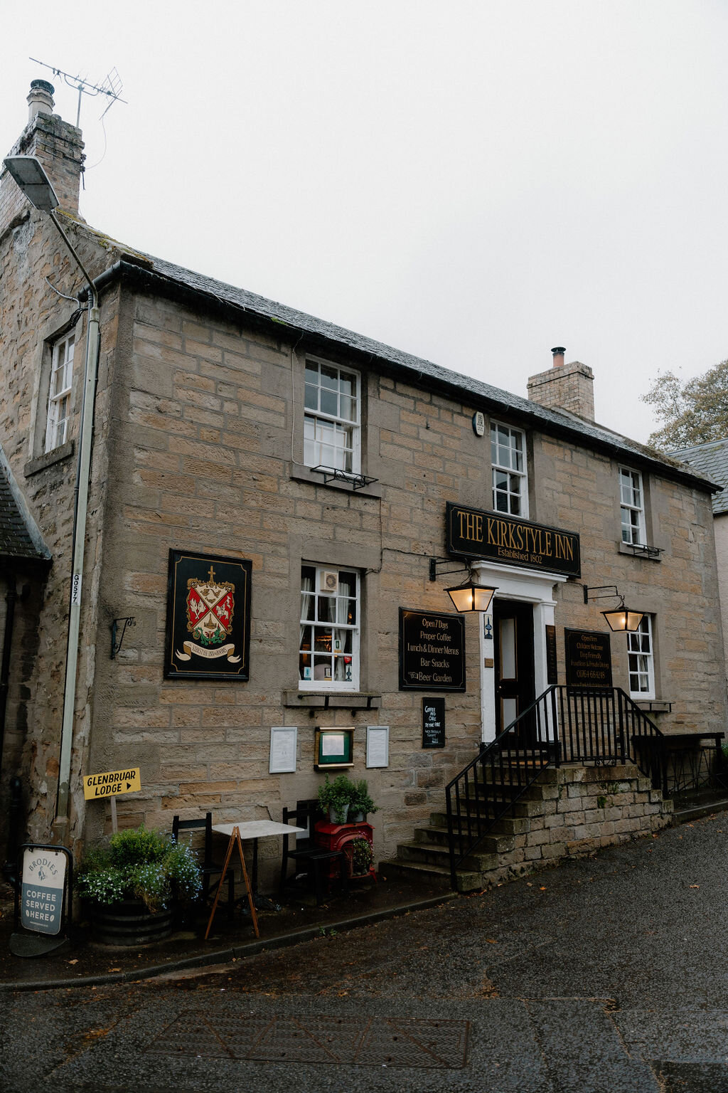 The Kirkstyle Inn's own sign and crest hang beside its entrance, a directional sign for Glenburgie Lodge nearby.