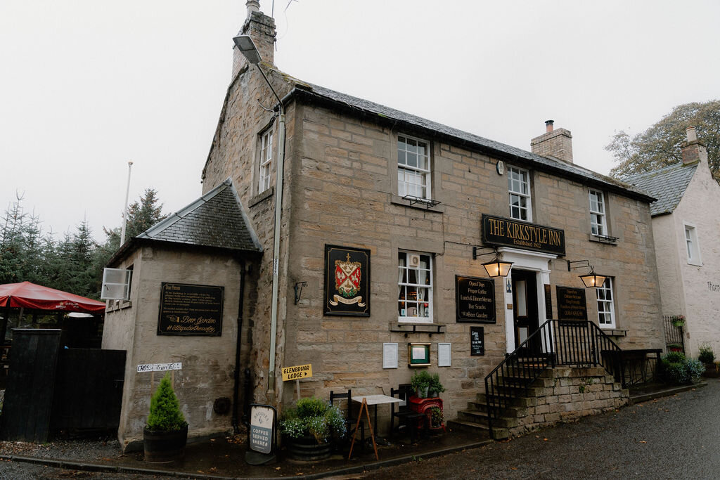 The Chandlery Inn's own sign and crest mark its stone frontage beside a red umbrella.
