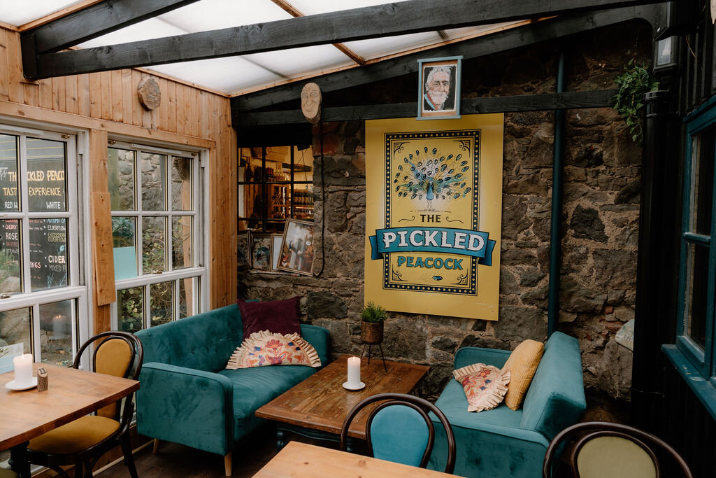 The Pickled Peacock's own poster hangs above teal velvet sofas in a stone-walled lounge.