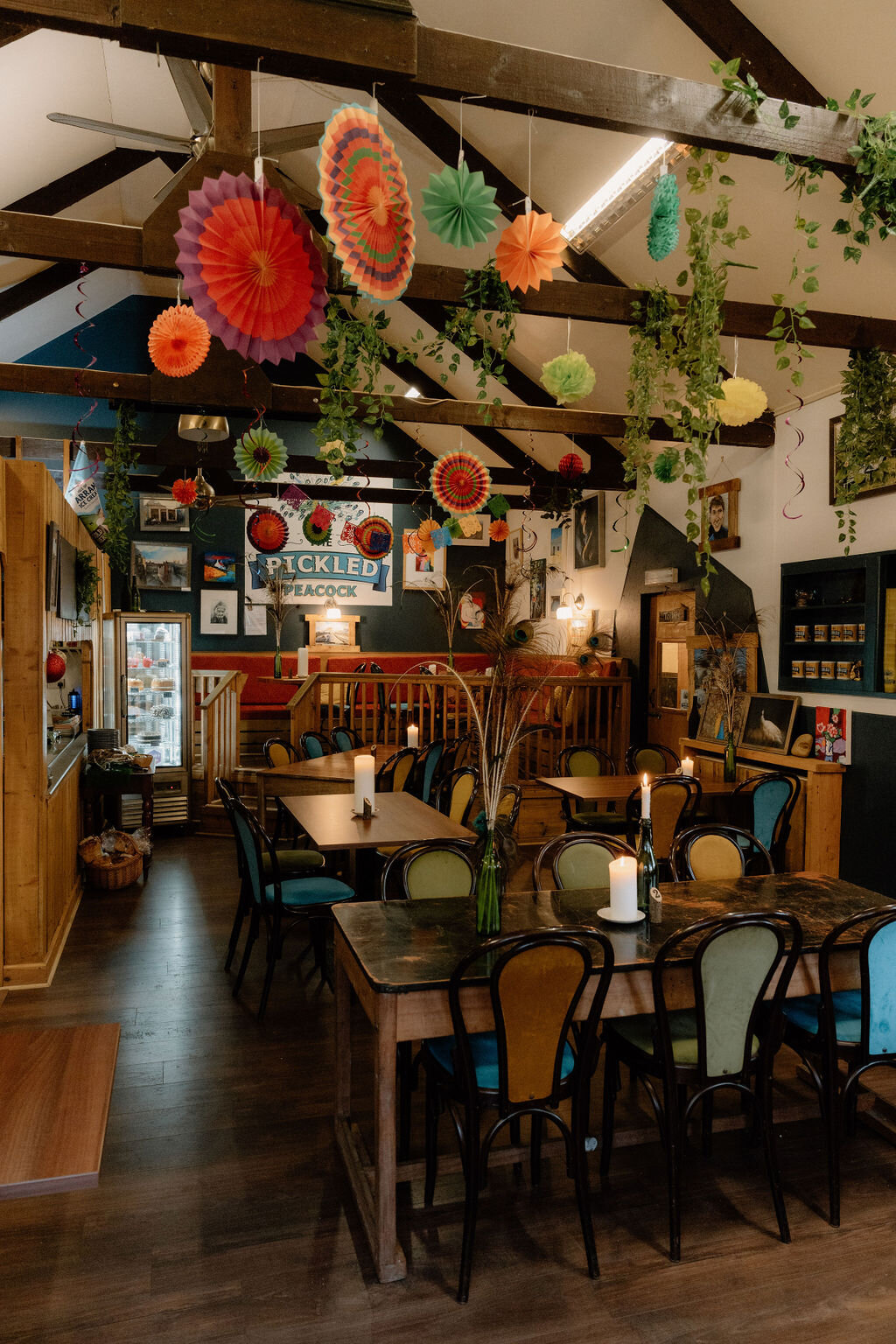 The Pickled Peacock's own sign hangs beneath colourful hanging fans and trailing plants.