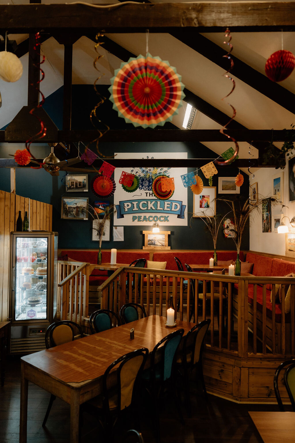 The Pickled Peacock's own sign hangs beneath colourful hanging fans and trailing plants.