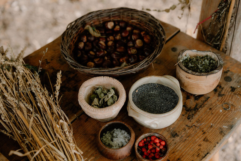 Foraged chestnuts, herbs and berries fill baskets and bowls on a wooden table.