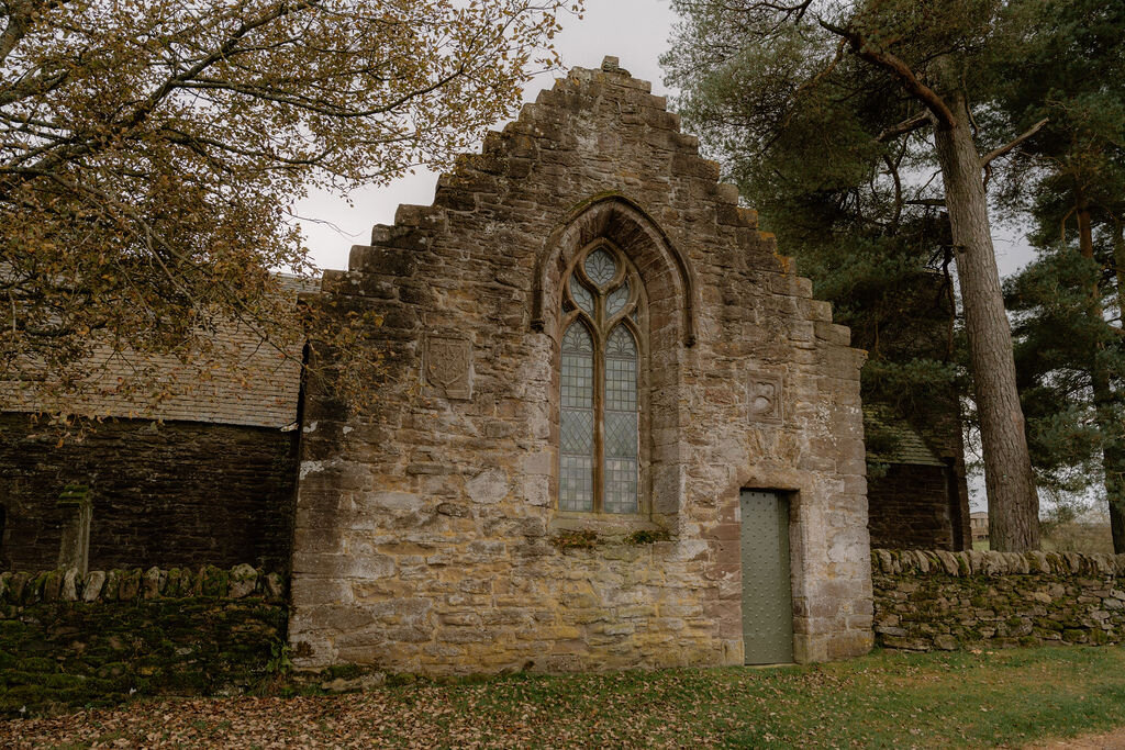 A stone church building with buttressed gables stands beside a grassy churchyard.