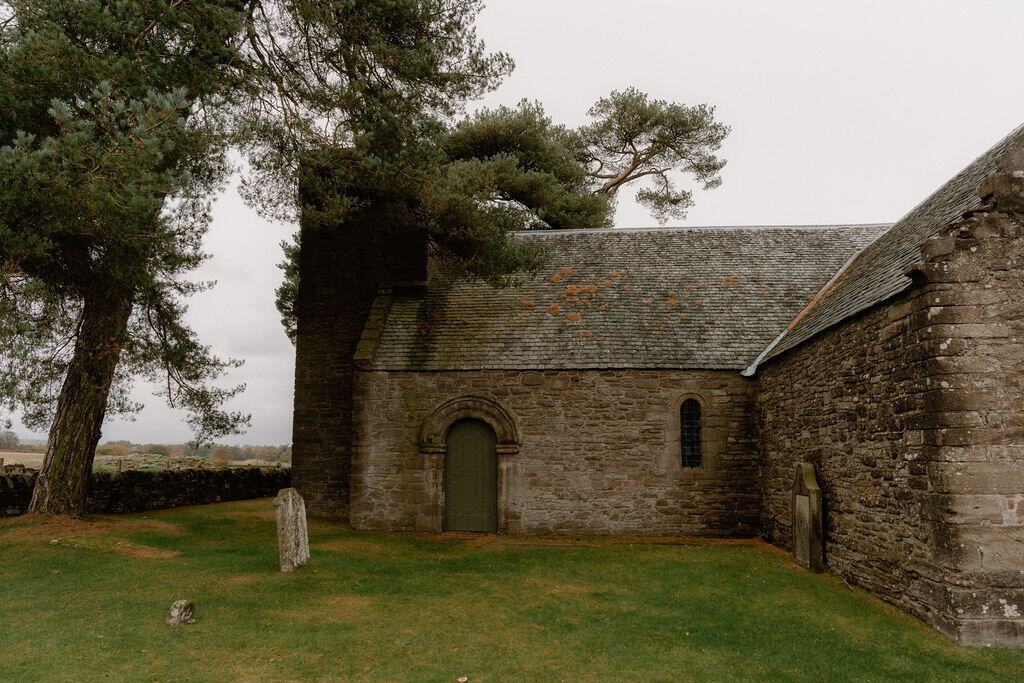 A stone church building with buttressed gables stands beside a grassy churchyard.