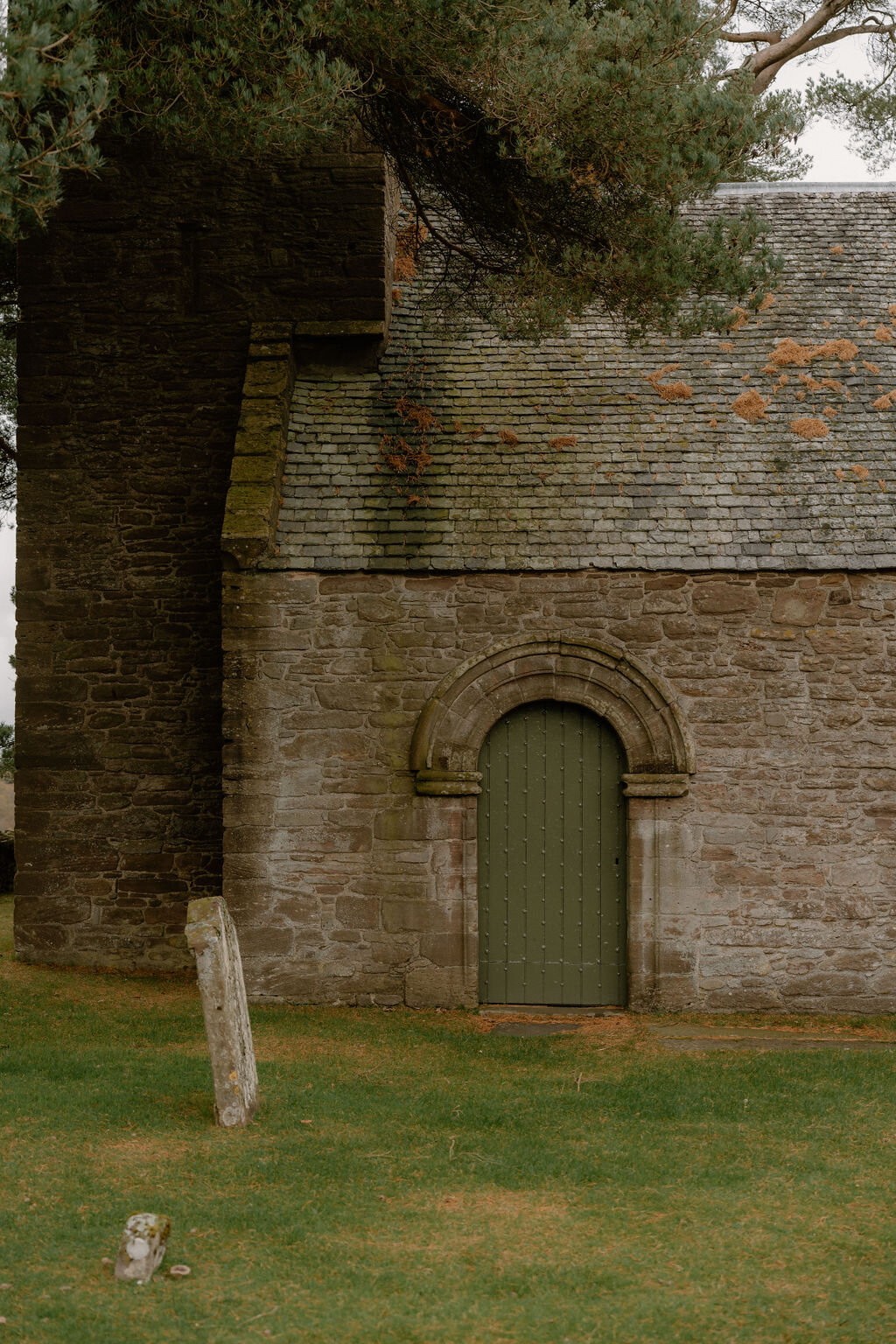 A green door sits beneath an arched stone surround on a moss-covered church wall.