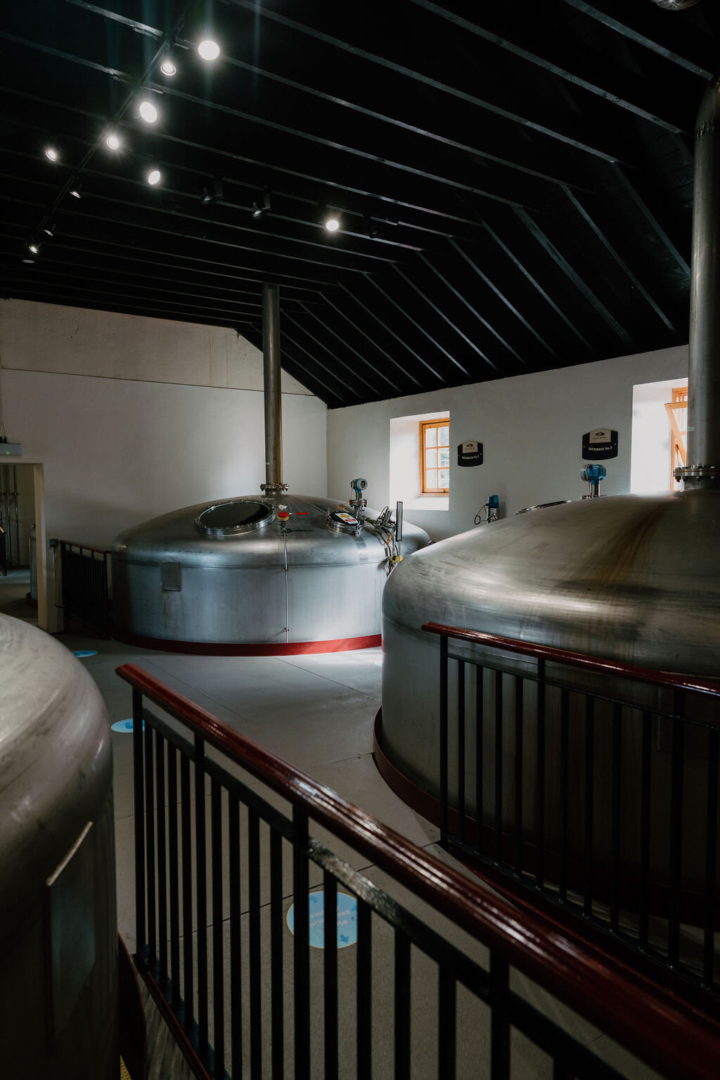 Steel washbacks stand behind a railing in a timber-roofed hall at a Perthshire distillery.