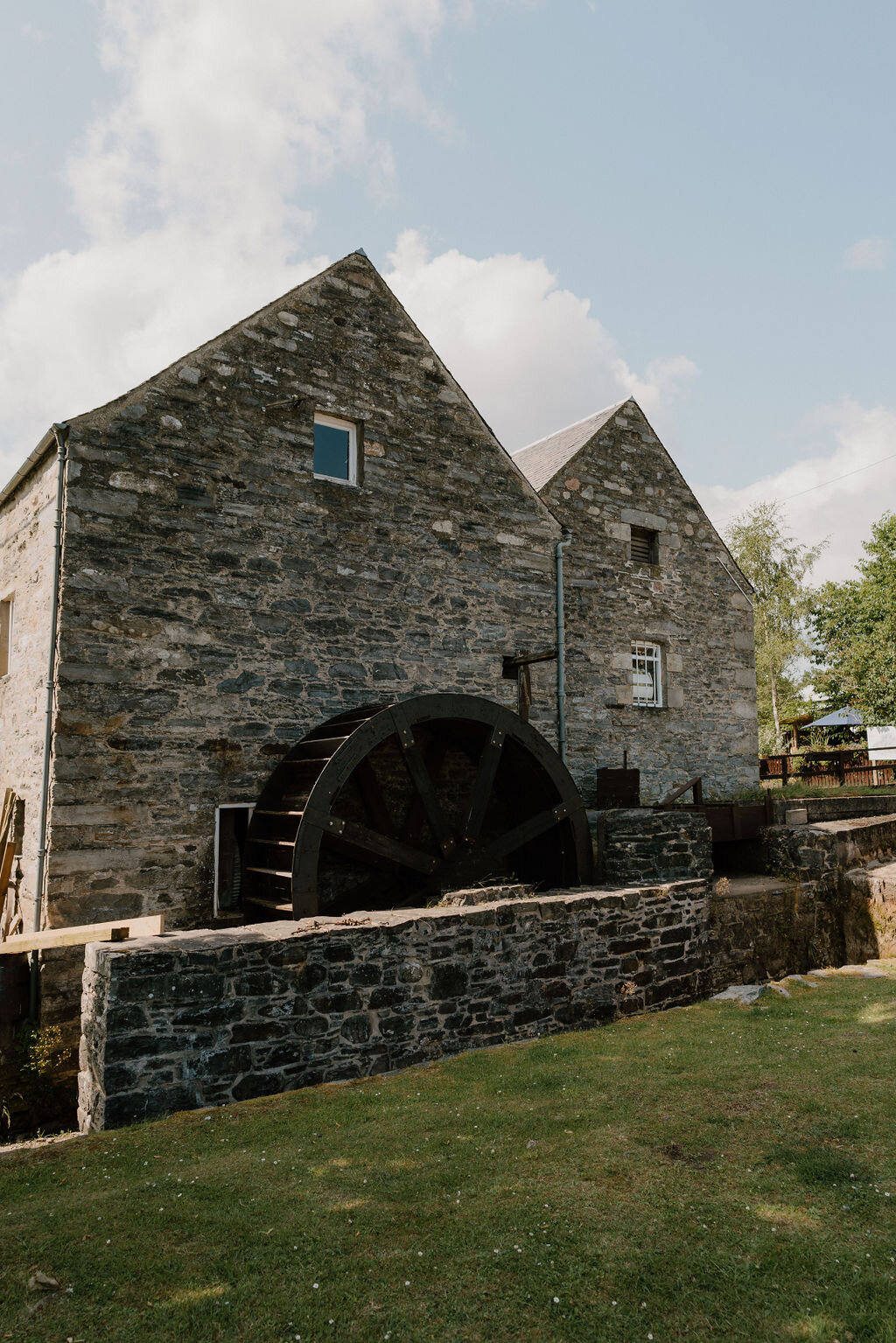 A stone watermill with a large wheel stands beside a low wall in Perthshire.
