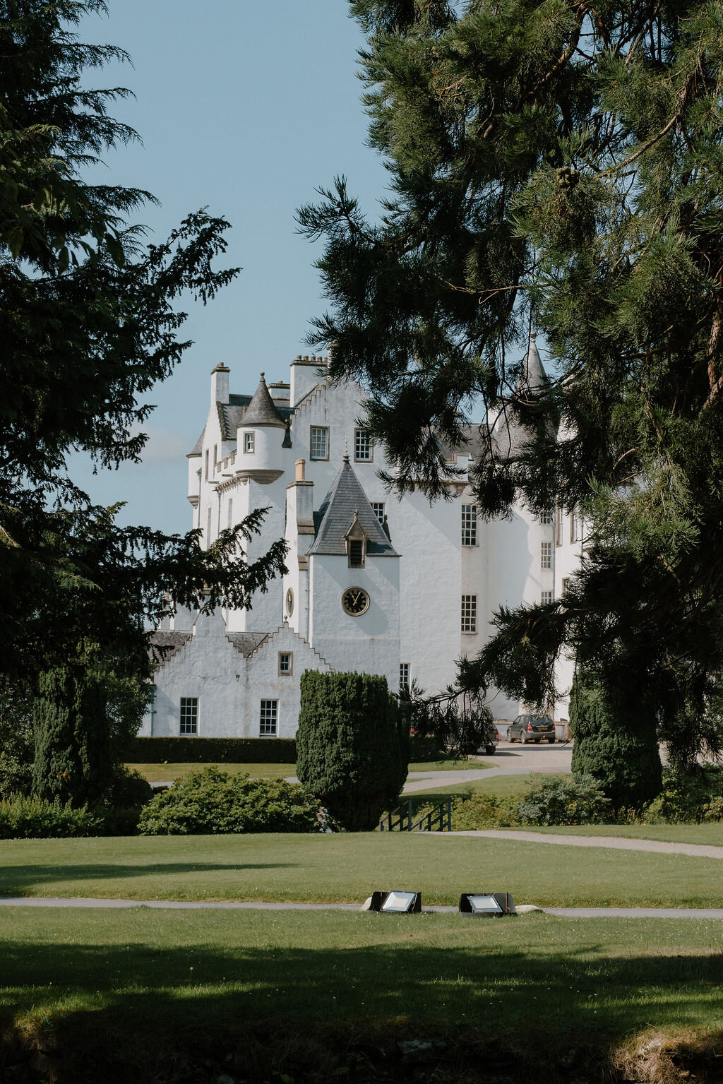 Blair Castle's white turreted towers rise above parkland trees and a clipped lawn.
