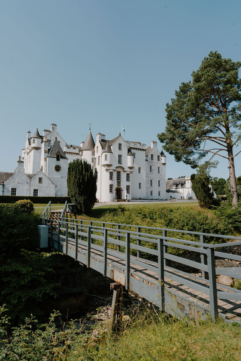 A wooden footbridge crosses a stream in front of Blair Castle's white turreted towers.