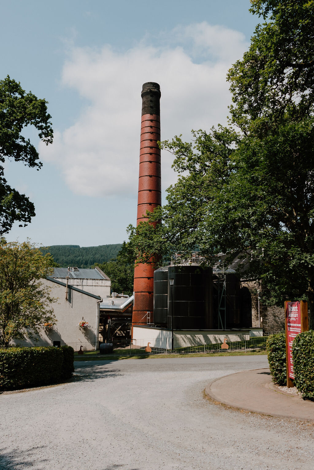 A tall red-brick chimney rises above storage tanks and stone buildings at Dewar's Aberfeldy distillery.