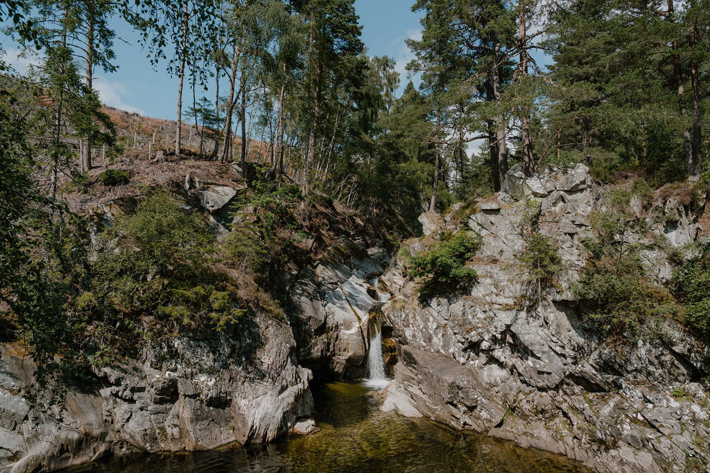 A waterfall drops into a rock pool at the foot of a wooded gorge.