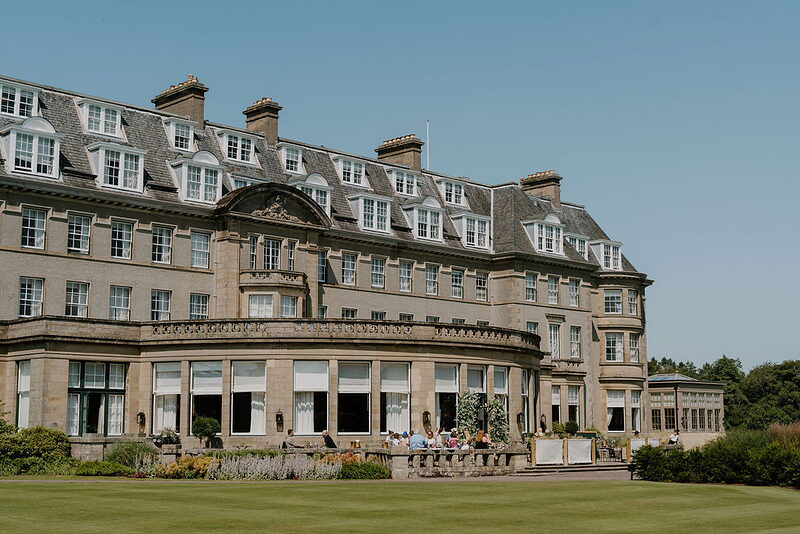 Gleneagles Hotel's long sandstone facade curves around a terrace with outdoor seating and a colonnade.