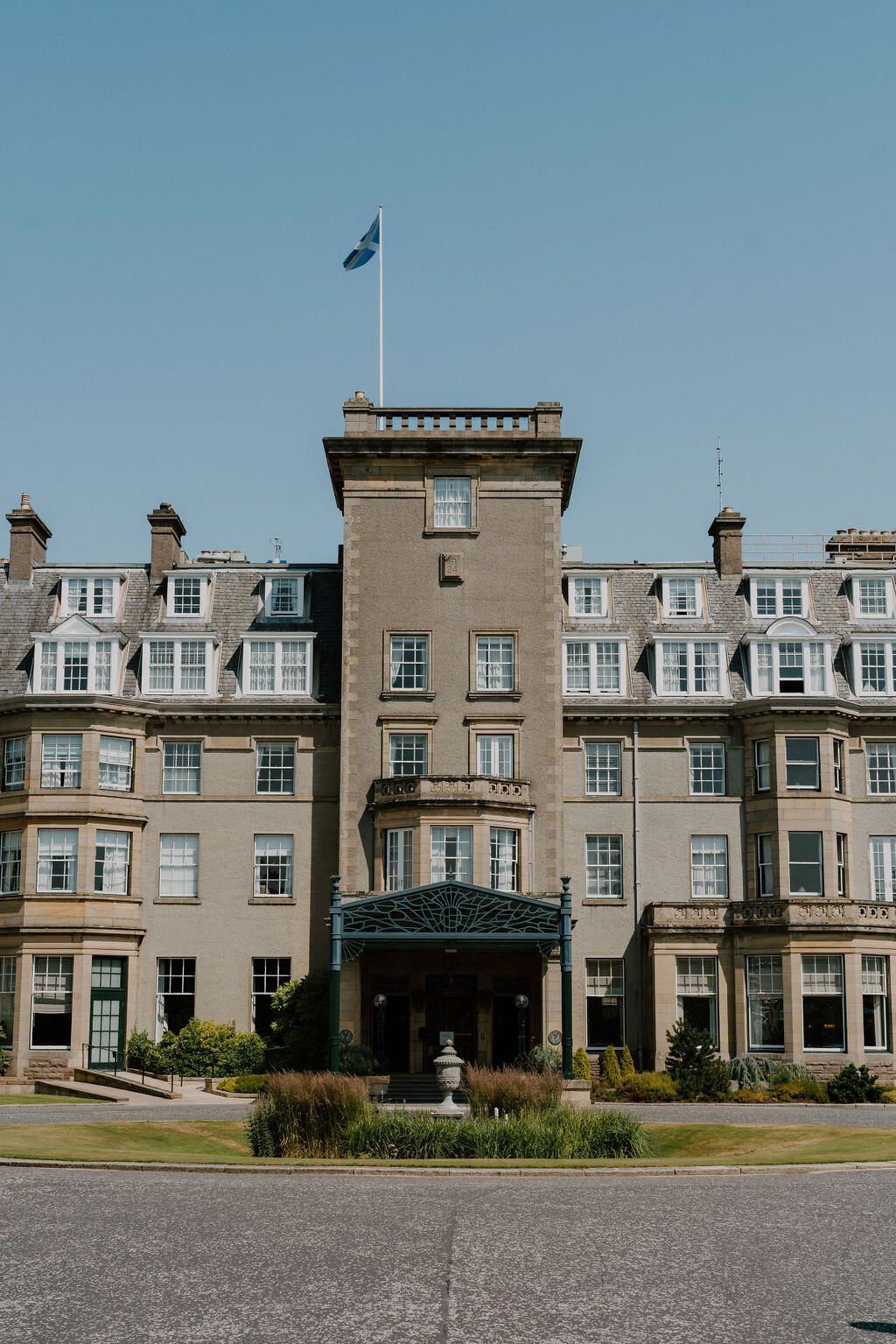 A Saltire flag flies above Gleneagles Hotel's central tower, framed by its symmetrical gabled wings.