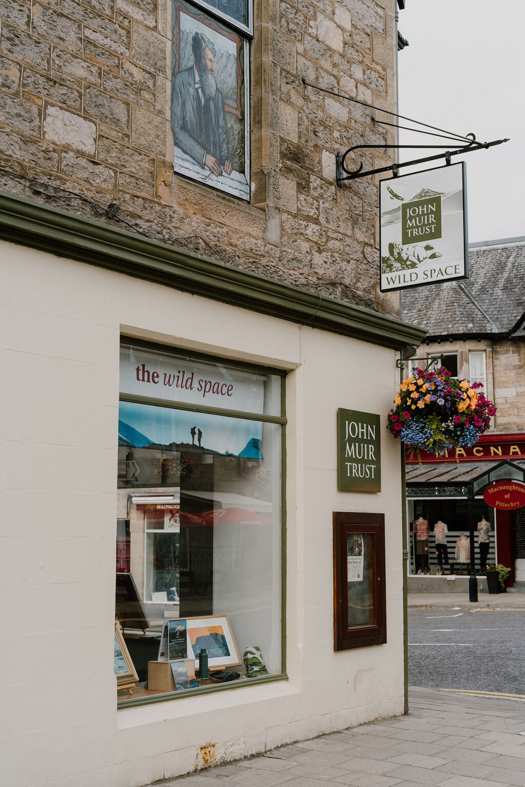 A hanging sign for the John Muir Trust's 'the wild space' gallery is mounted beside a painted stone building.