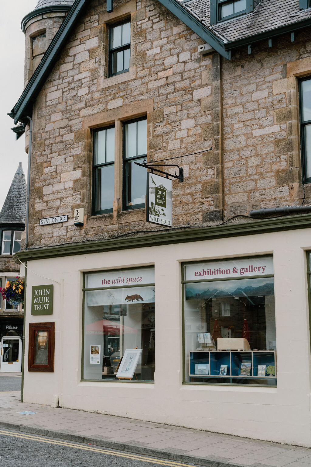 The Wild Space exhibition and gallery's window display sits beneath a hanging John Muir Trust sign on Station Road.