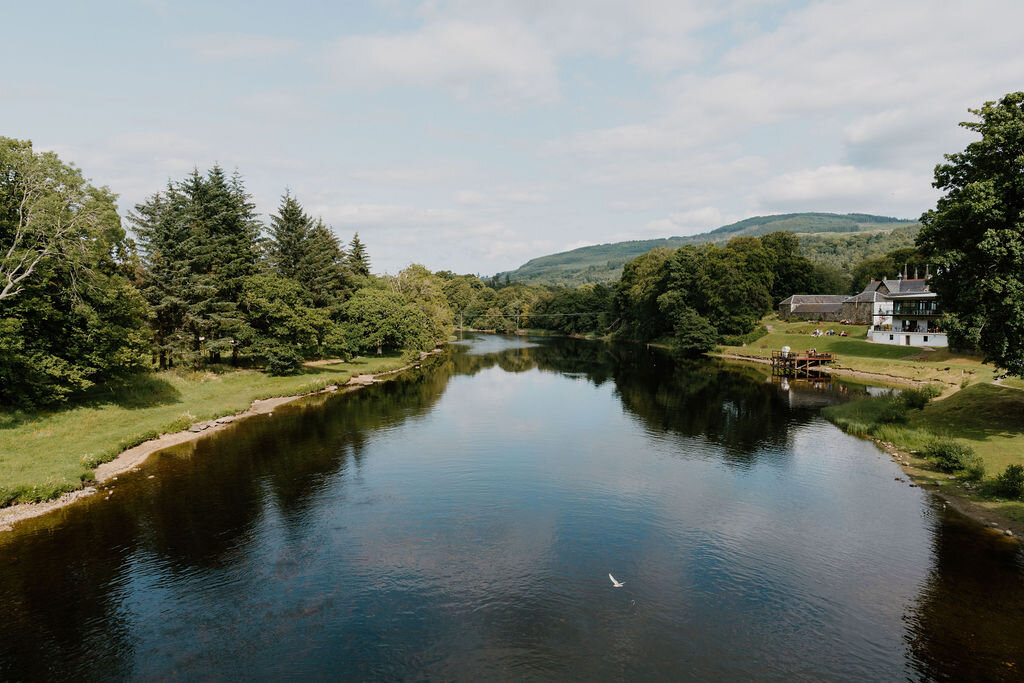 The River Tay flows past a white house and jetty beneath wooded hills near Kenmore.