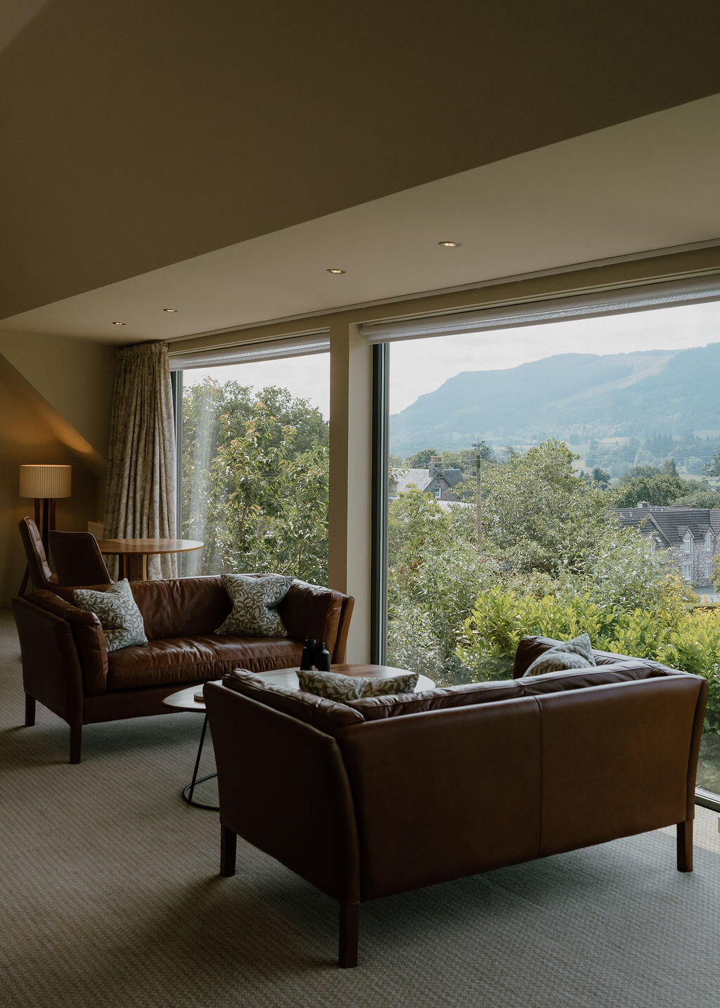 Leather sofas face a low table beneath a large window overlooking wooded hills.