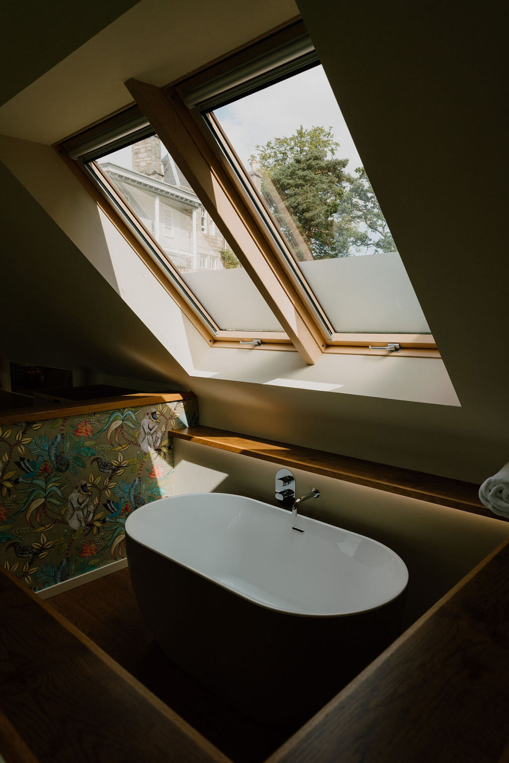 A freestanding bathtub sits beneath a skylight window with a floral-tiled surround.