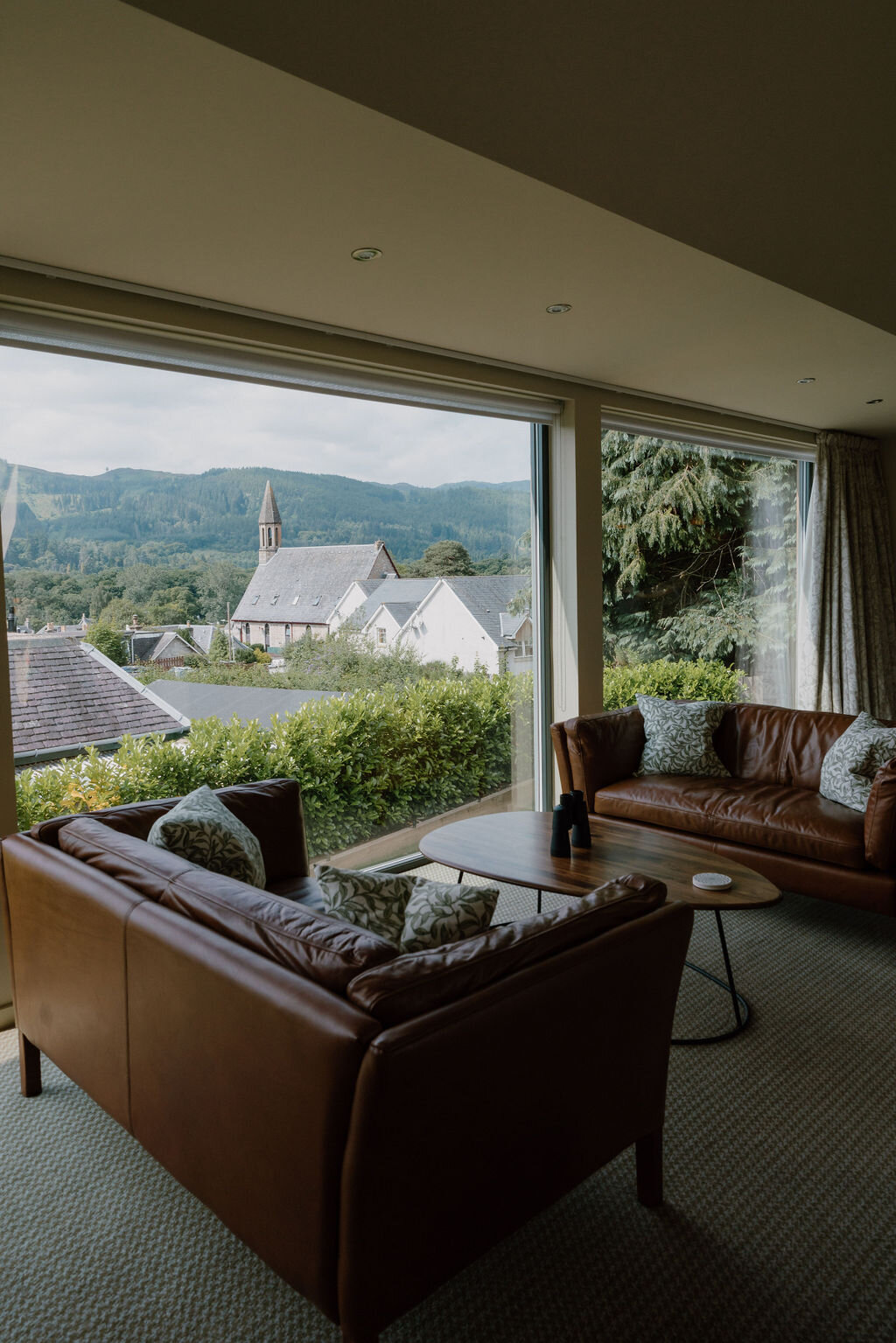 Leather sofas and a coffee table face a picture window overlooking a village and church spire.