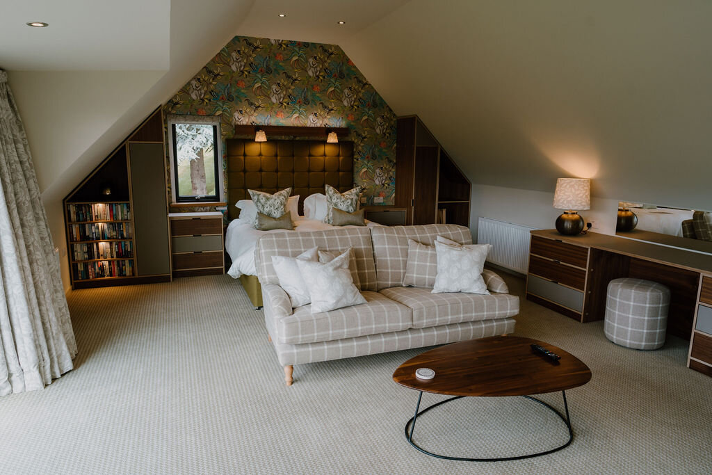 A bed with patterned tiger-motif wallpaper sits beneath a sloped ceiling behind a checked sofa.