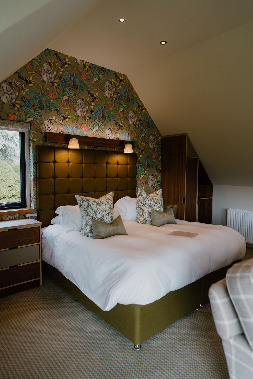 A bed with patterned tiger-motif wallpaper and a padded headboard sits beneath a sloped ceiling.