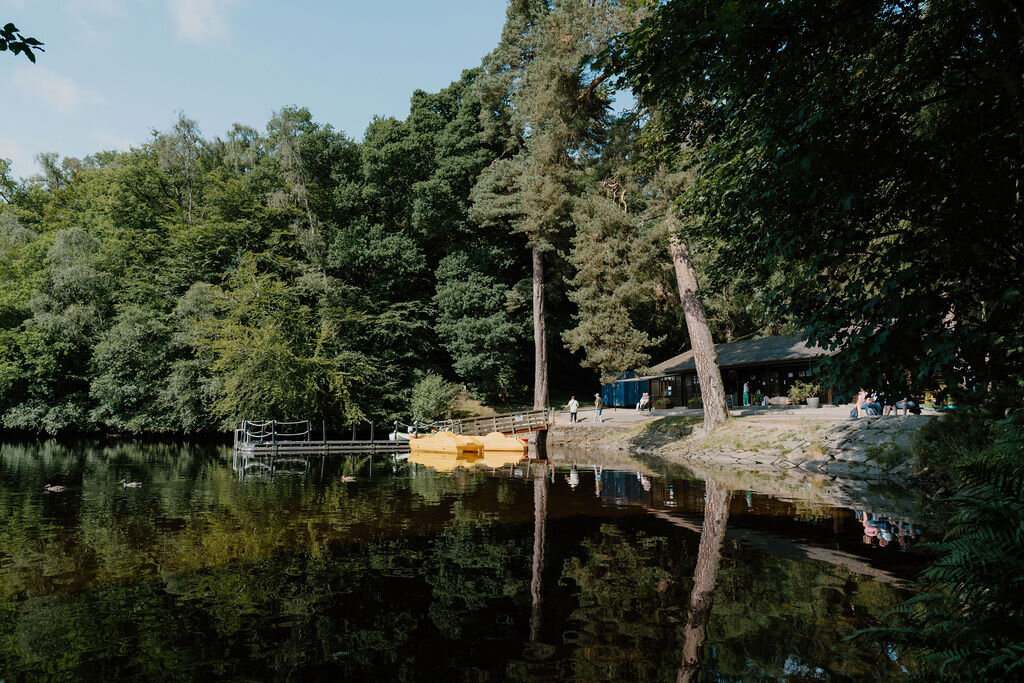 A yellow pedalo is moored beside a jetty on a wooded loch near a log cabin building.