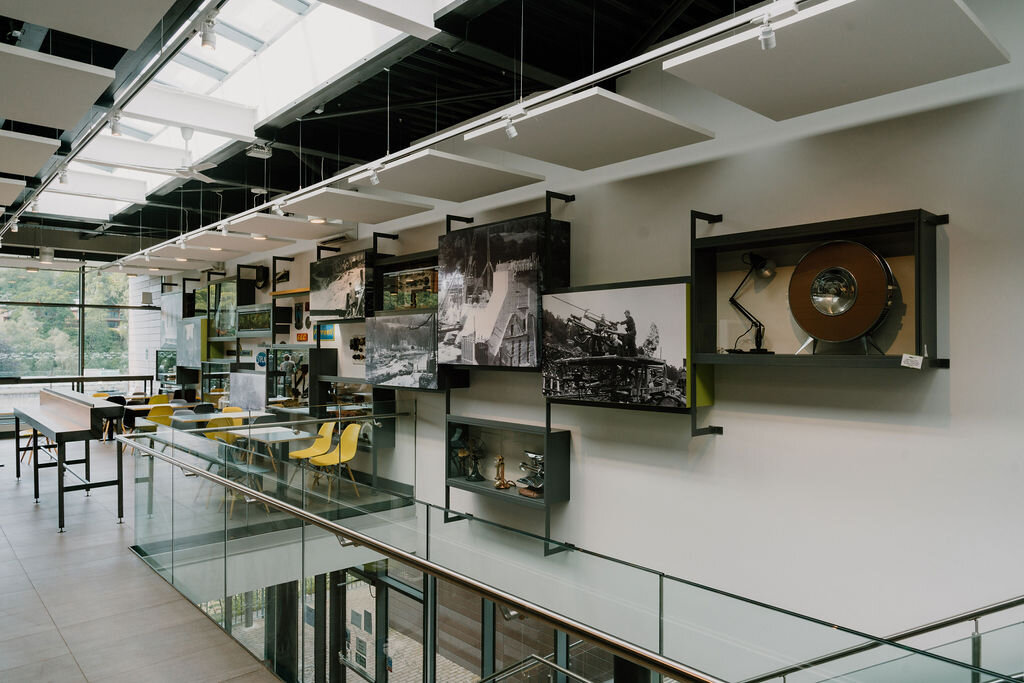 Framed historical photographs and museum artefacts line a glass-railed mezzanine at the Pitlochry Dam visitor centre.