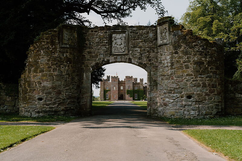 A stone archway frames a distant view of Scone Palace's turreted facade.