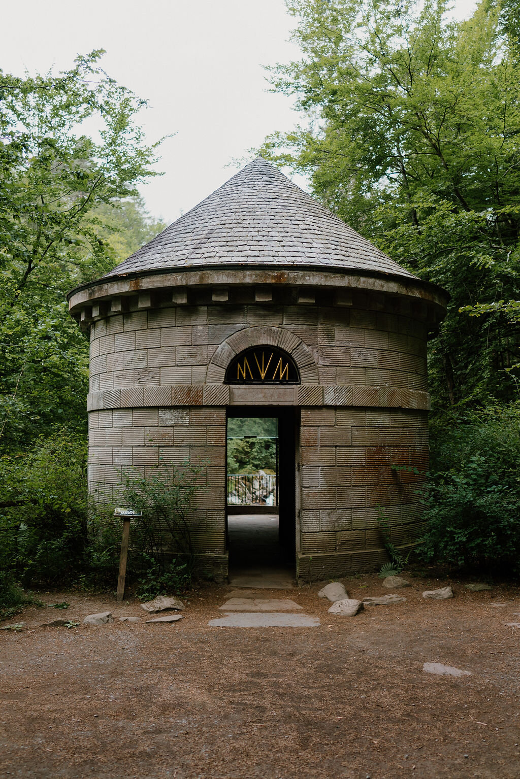 A round stone folly with a carved MVM monogram over its doorway stands in a Perthshire wood, its conical roof rising above the trees.