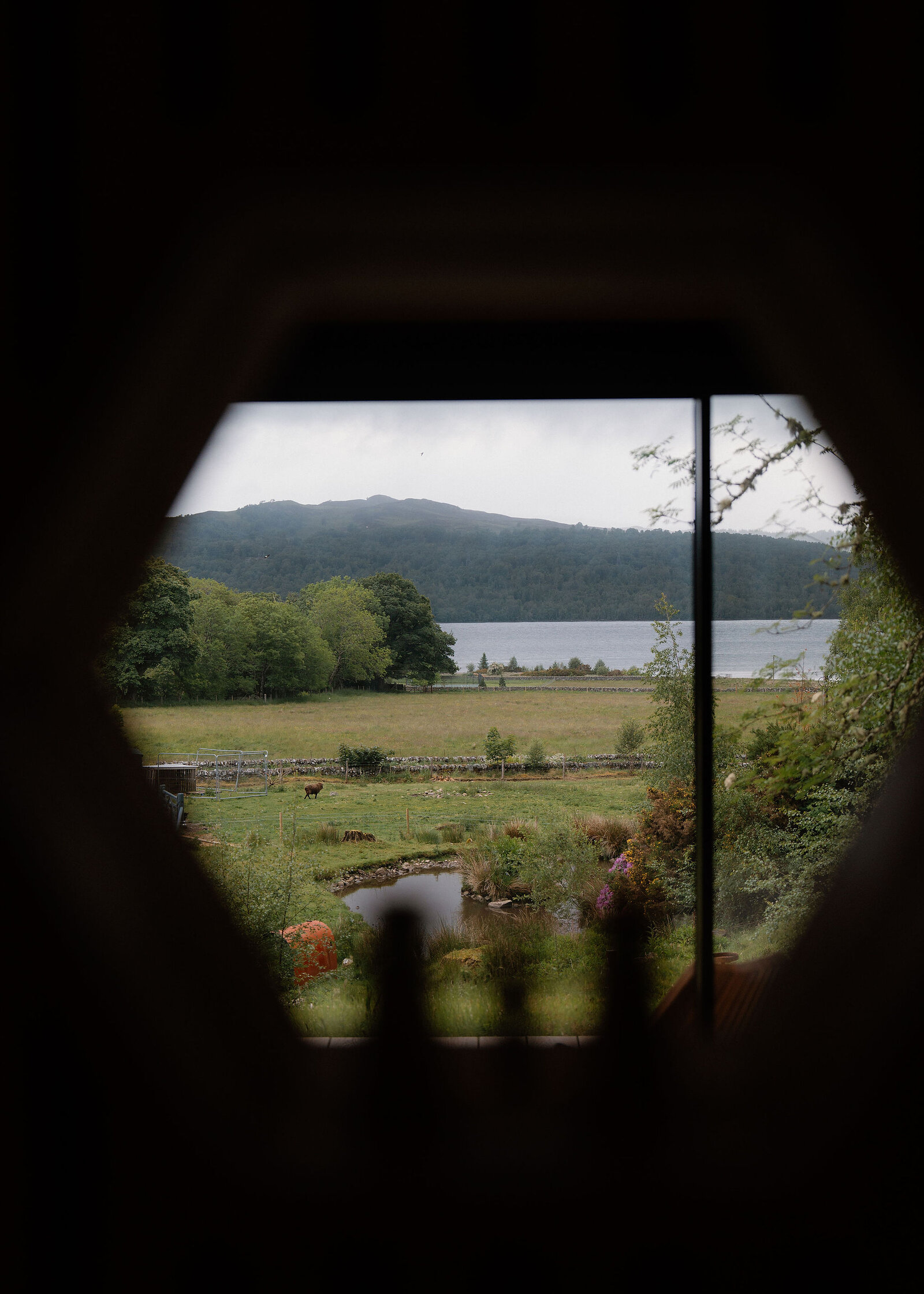 Fields, a pond and Loch Rannoch framed by a hexagonal opening in the dark, like a window cut in the wall.