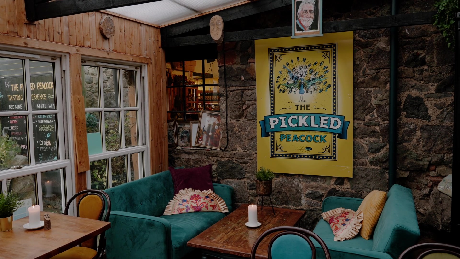 The Pickled Peacock's peacock sign hangs on a stone wall above teal sofas and candlelit tables, a drinks chalkboard in the window.