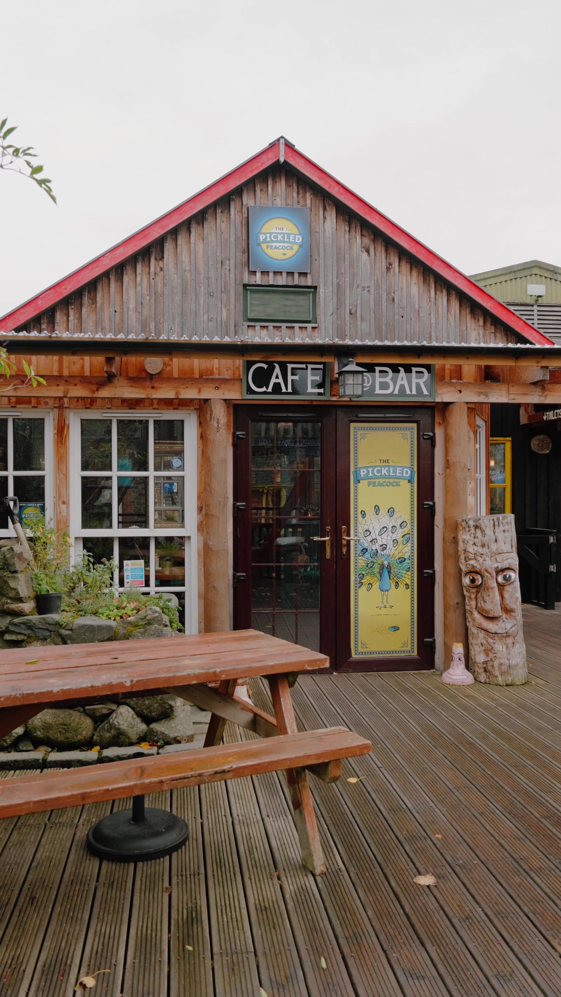 The Pickled Peacock's cafe and bar entrance, a peacock illustration on the door and a carved wooden face beside it.